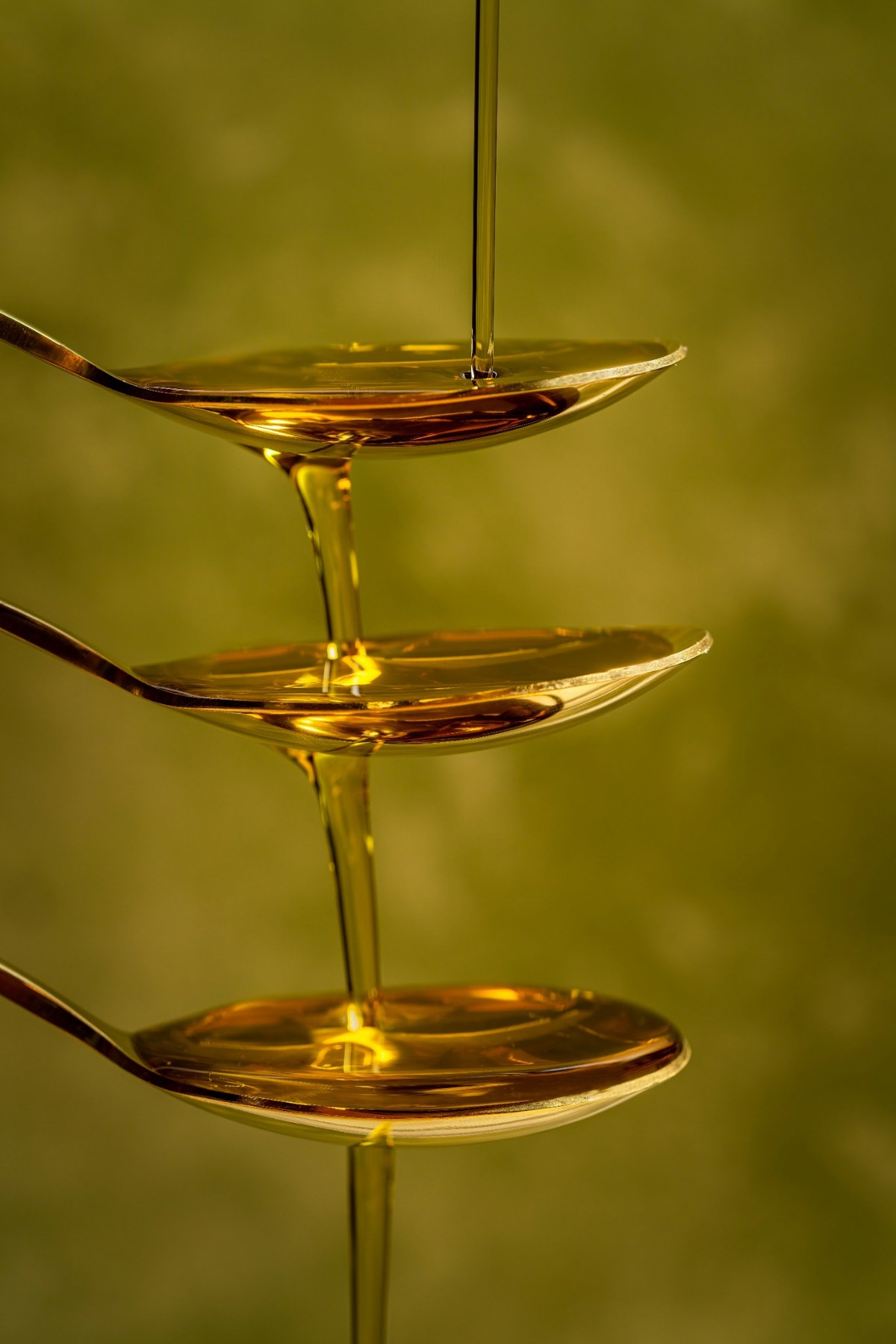 Golden oil cascading over three stacked spoons